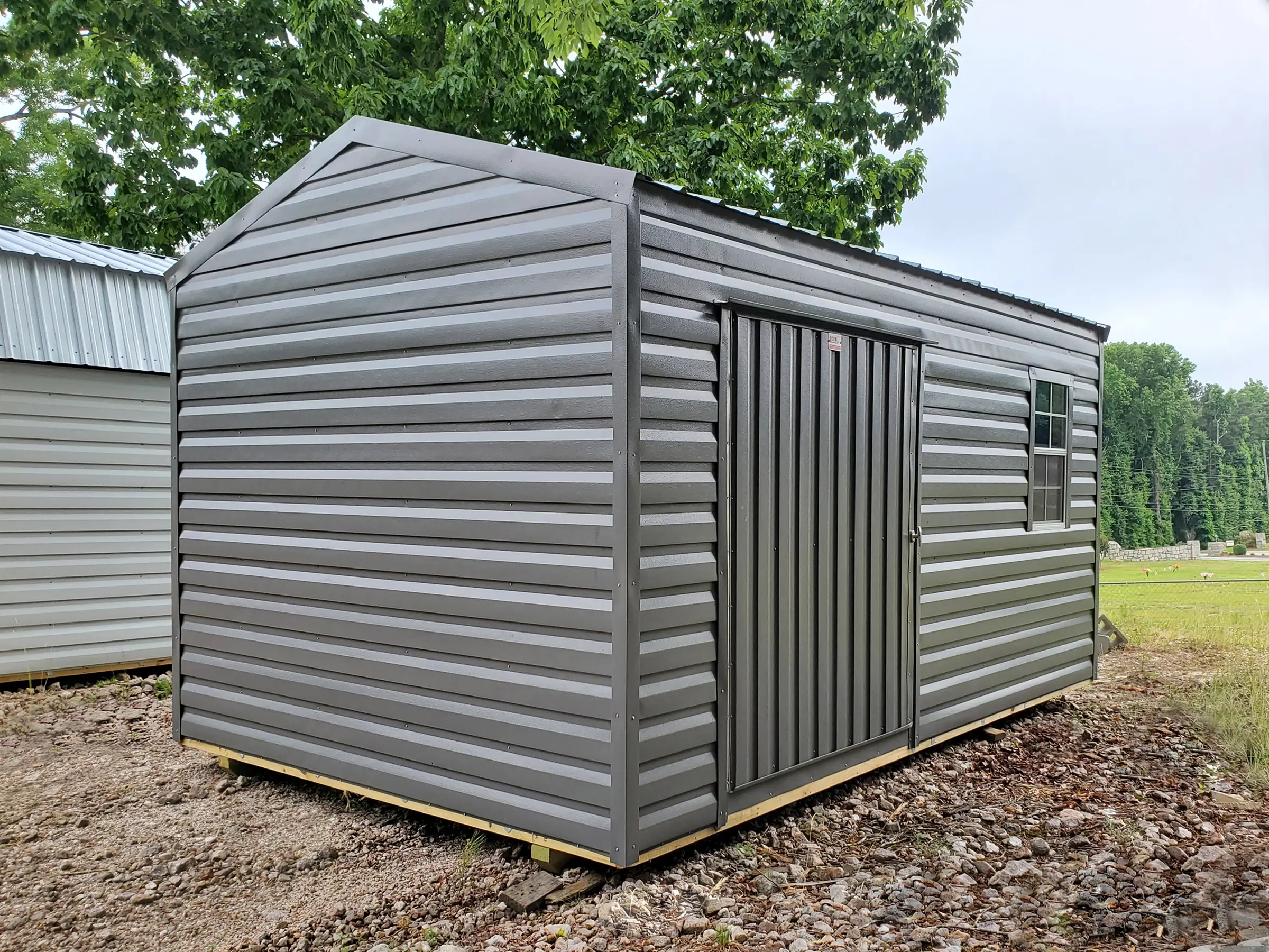 This all gray 10 by 16 portable shed building is equipped with a window and large door for riding mowers.